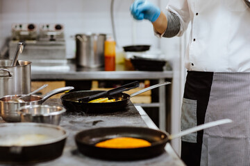 Cook in uniform frying potato in skillet on the restaurant's kitchen. 