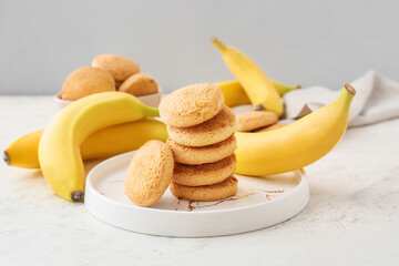 Plate with tasty cookies and bananas on light background