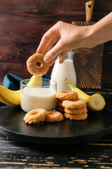 Female hand with tasty banana cookie and milk on dark wooden background