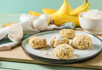 Plate with uncooked banana cookies and ingredients on color wooden background
