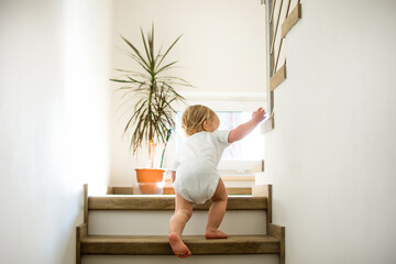 Little caucasian baby is crawling on stairs at home in sunny interior. Lifestile photography....