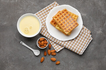 Bowl with sweet condensed milk, almonds and waffles on dark background