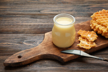 Jar with sweet condensed milk and waffles on wooden background