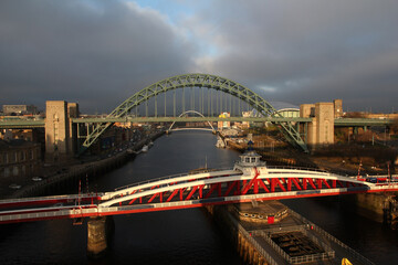 Fototapeta na wymiar Dark storm clouds behind the Millennium and Tyne Bridges which are lit in a golden light by the sun breaking through the clouds