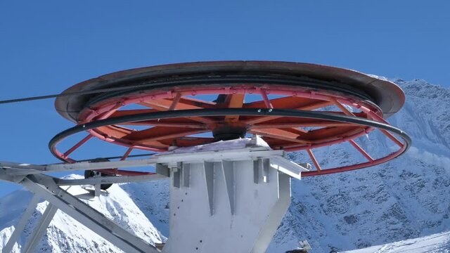 Huge colorful reel with cable rotates to move cabins of modern poma lift at ski resort against large mountains in winter