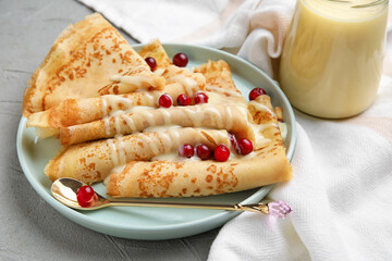 Plate with thin pancakes, cranberries and condensed milk on grey background