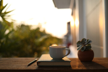 White cup and notebook on wooden table under sunset light