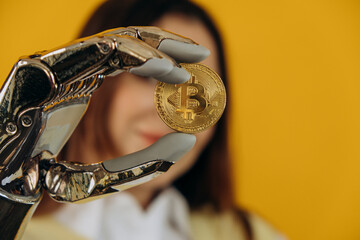 Lady with modern shiny metal bionic arm holds large golden bitcoin posing for camera on yellow...