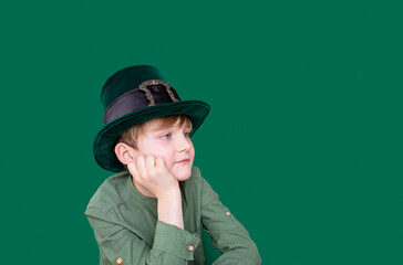 A closeup portrait of dreamy preteen boy in carnival St. Patrick's Day hat on green backgroundwhite. Copy space.