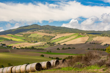Sunny day landscape rural view, Tuscany, Italy. Bales of straw in line in the foreground. Vivid...