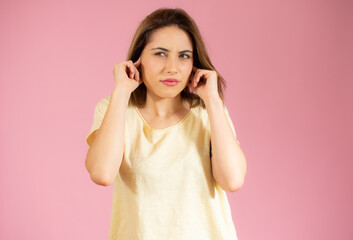 Young beautiful woman wearing casual t-shirt standing over isolated pink background covering ears with fingers with annoyed expression. Deaf concept.