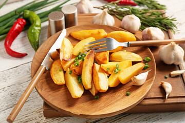 Plate of tasty baked potato with garlic on light wooden background
