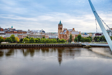Derry, Ireland. Illuminated Peace bridge in Derry Londonderry, City of Culture, in Northern Ireland with city center at the background. Night cloudy sky with reflection in the river at the dusk