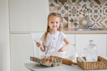 Portrait of a little cute smiling girl. Childrens hands kneading dough on the table in the art nouveau kitchen. Preparing for Easter baking. Biscuits.