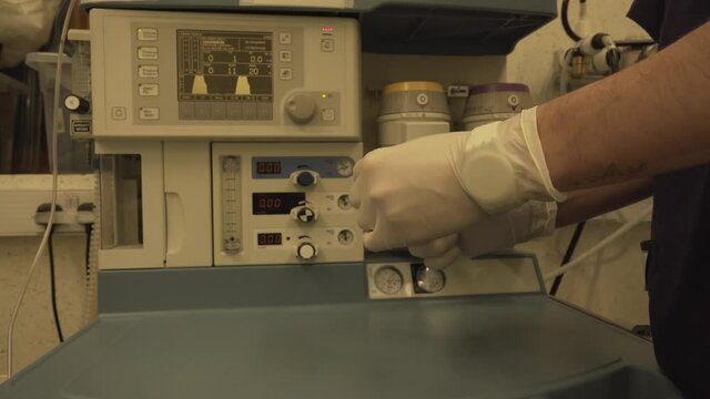 Anaesthetist Preparing Drug Syringe In Front Of Anaesthetic Machine Workstation For Patient With Coronavirus In Hospital