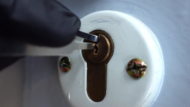 Burglar Wearing Black Latex Gloves Attempting To Pick Brass Pin Tumbler Door Lock with Lockpicking Tools Close Up
