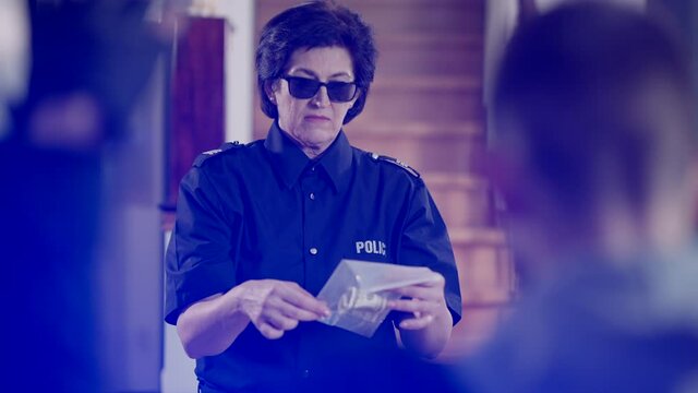 Caucasian female police officer in sunglasses holding transparent package with money as unknown criminal burglar with raised hands standing at front. Policewoman collects evidence of robbery.