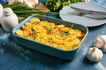 Baking dish of tasty potato with cheese and garlic on color background