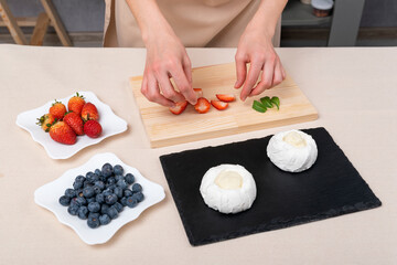 Obraz na płótnie Canvas Woman prepares cakes using strawberries, blueberries and meringue. Cake Anna Pavlova