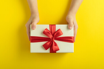 Childrens hands are holding gift on yellow background. Top view.