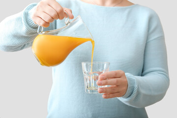 Woman pouring healthy turmeric drink from jug into glass on light background
