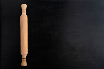 Wooden rolling pin on black background, top view. Copy spac. Kitchen concept