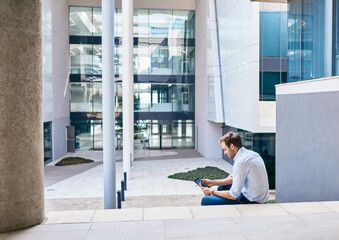 Young businessman using a tablet outside on office steps