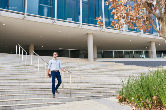 Smiling Businessman Walking Down Stairs Outside Of An Office Building