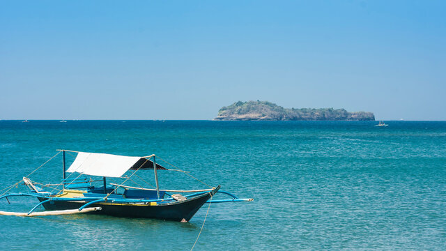 A small tourist outrigger boat is moored near Calayo Beach, while Loren island is visible in the background. A popular beach and island hopping area for local tourists. In Nasugbu, Philippines.
