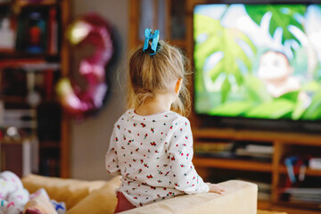 Cute little toddler girl in nightwear pajamas watching cartoons or movie on tv. Happy healthy baby...