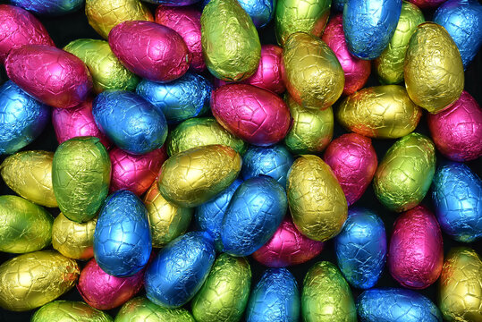 Pile or group of multi colored colourful foil wrapped chocolate easter eggs in pink, blue, yellow and lime green. - Powered by Adobe