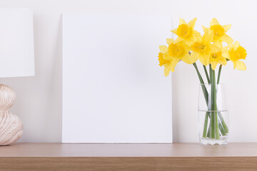 Breakfast still life., empty picture frame mockup on wooden desk, table. Vase with daffodils branches. Elegant working space, home office concept. Scandinavian interior design
