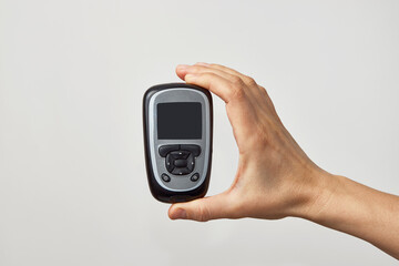 Hand holding glucometer with blood sugar test result.