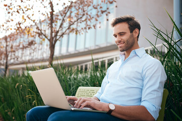 Smiling businessman using a laptop outside of an office building
