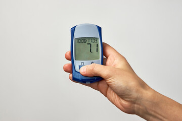 Hand holding glucometer with blood sugar test result.