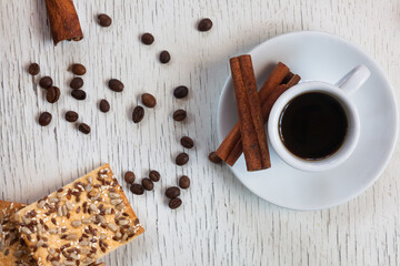 A mug of aromatic coffee with coffee beans, oatmeal cookies and cinnamon sticks on a white antique table. View from above.