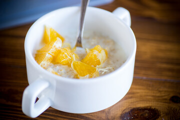 cooked boiled sweet oatmeal with oranges in a bowl