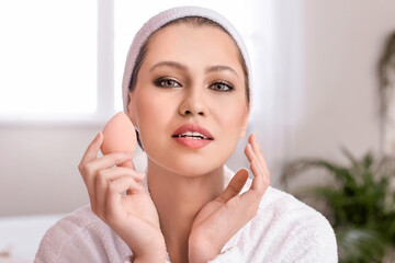 Beautiful young woman with sponge applying makeup at home