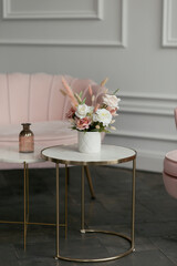 A beautiful bouquet of white and pink flowers stands on a stylish coffee table against the backdrop of a sofa
