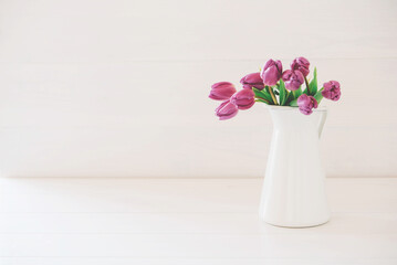 Beautiful mono bouquet of purple tulips in full bloom in white vase on white background. Copy space for text. Spring still life.