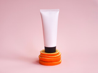 Mockup of pink squeeze bottle plastic tube with black cap on orange slices stand on pink...