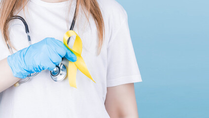 Female doctor holding yellow ribbon awareness symbol for suicide, sarcoma bone cancer, bladder cancer, liver cancer and childhood cancer concept. Health care.