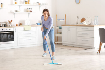 Young woman mopping floor in kitchen