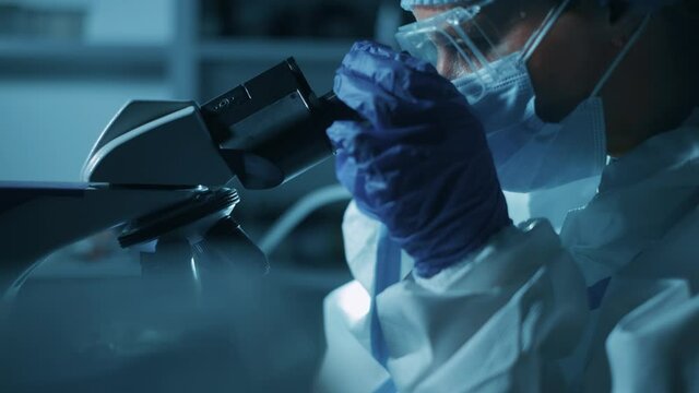 Woman scientist is looking into microscope. Biochemical research scientist is working with microscope for coronavirus vaccine development in pharmaceutical research laboratory