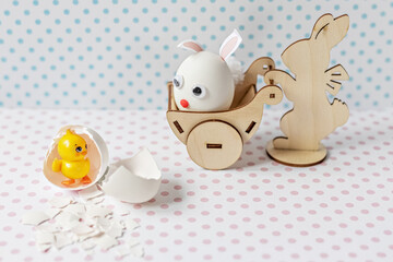 Wooden rabbit carrying a cart with an egg with bunny ears and a muzzle. Eggshell with a hatched chick.