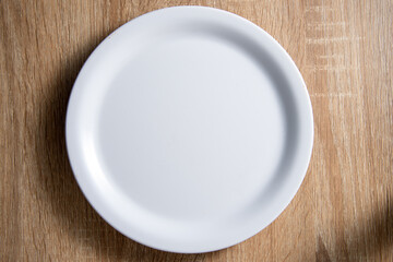 empty white round dish lay on wood table with soft shadow