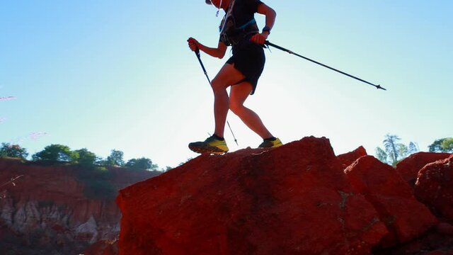 man trail runner climb rock using trekking poles
