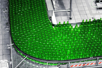 Automated conveyor line in a brewery. Rows of green glass bottles on a conveyor belt. Industrial...
