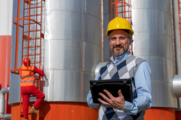 Manager or Engineer With Digital Tablet Standing in front of Oil Refinery Storage Tanks