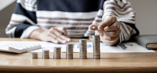 Women are stacking coins on top of the coin pile on the highest row. Placing coins in a row from low to high is comparable to saving money to grow more. Money saving ideas for investing in funds.